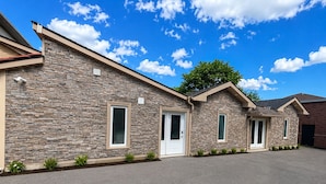 A two-story building with a stone facade, a driveway, and a tree in the background.