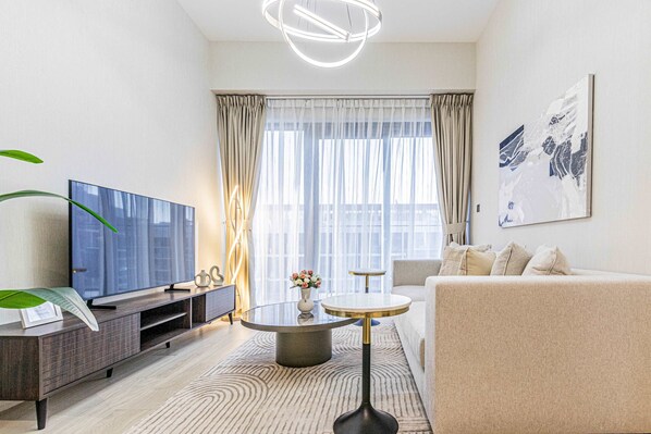A modern living room with a flat-screen TV, a sofa, a coffee table, and a large window with curtains.