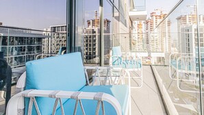 En balkon med en blå stol, et lille bord og gelænder af glas.