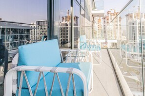 A balcony with a blue chair, a small table, and a glass railing.