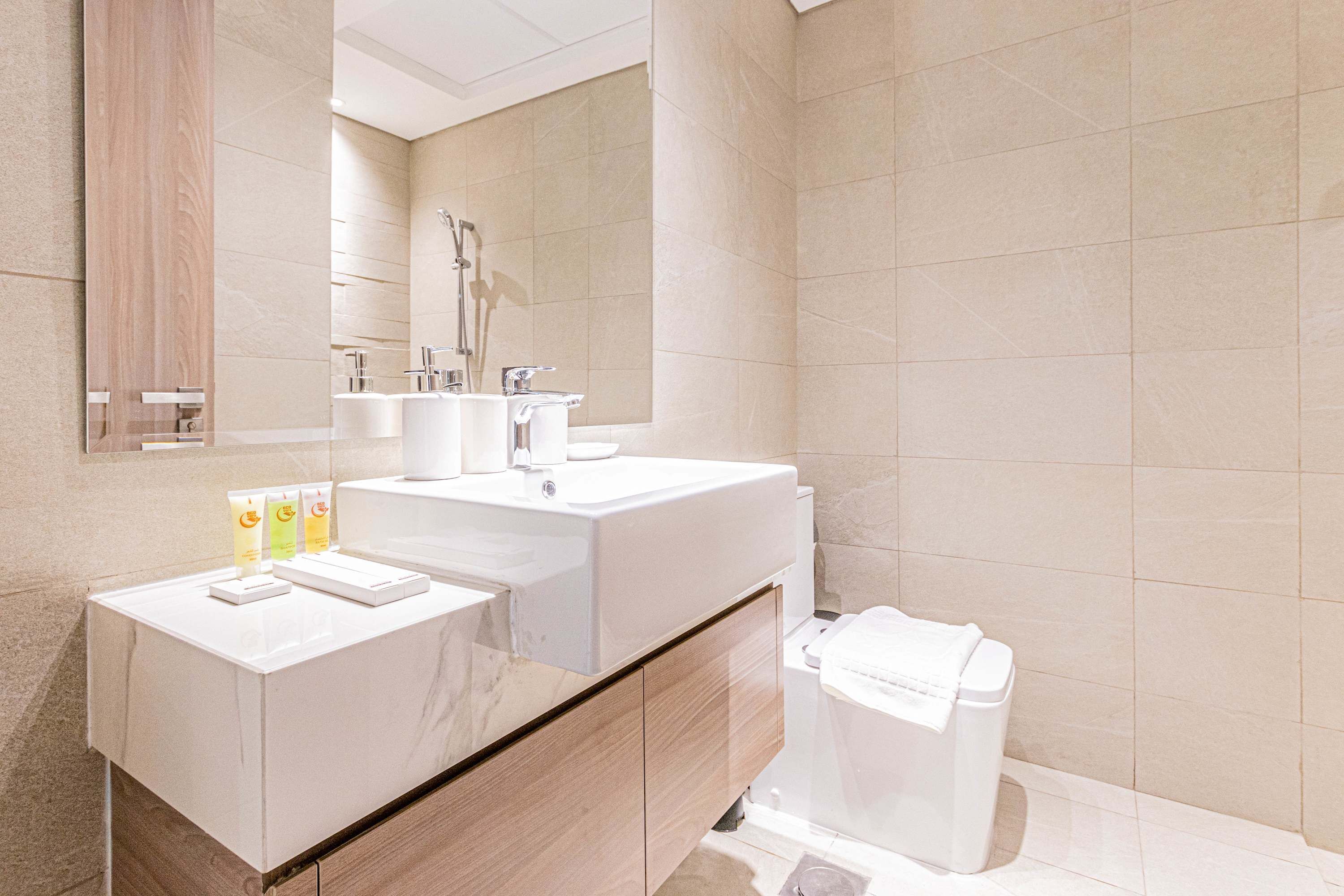 A modern bathroom with a large mirror, two sinks, a shower, and a toilet.