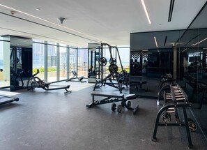 A modern gym with various exercise equipment, large windows, and a view of the city.