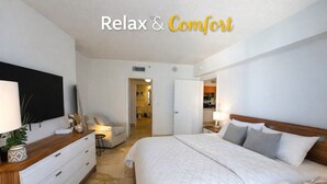 A bedroom with a bed, bedside tables, a TV, and a bathroom visible through an open door.