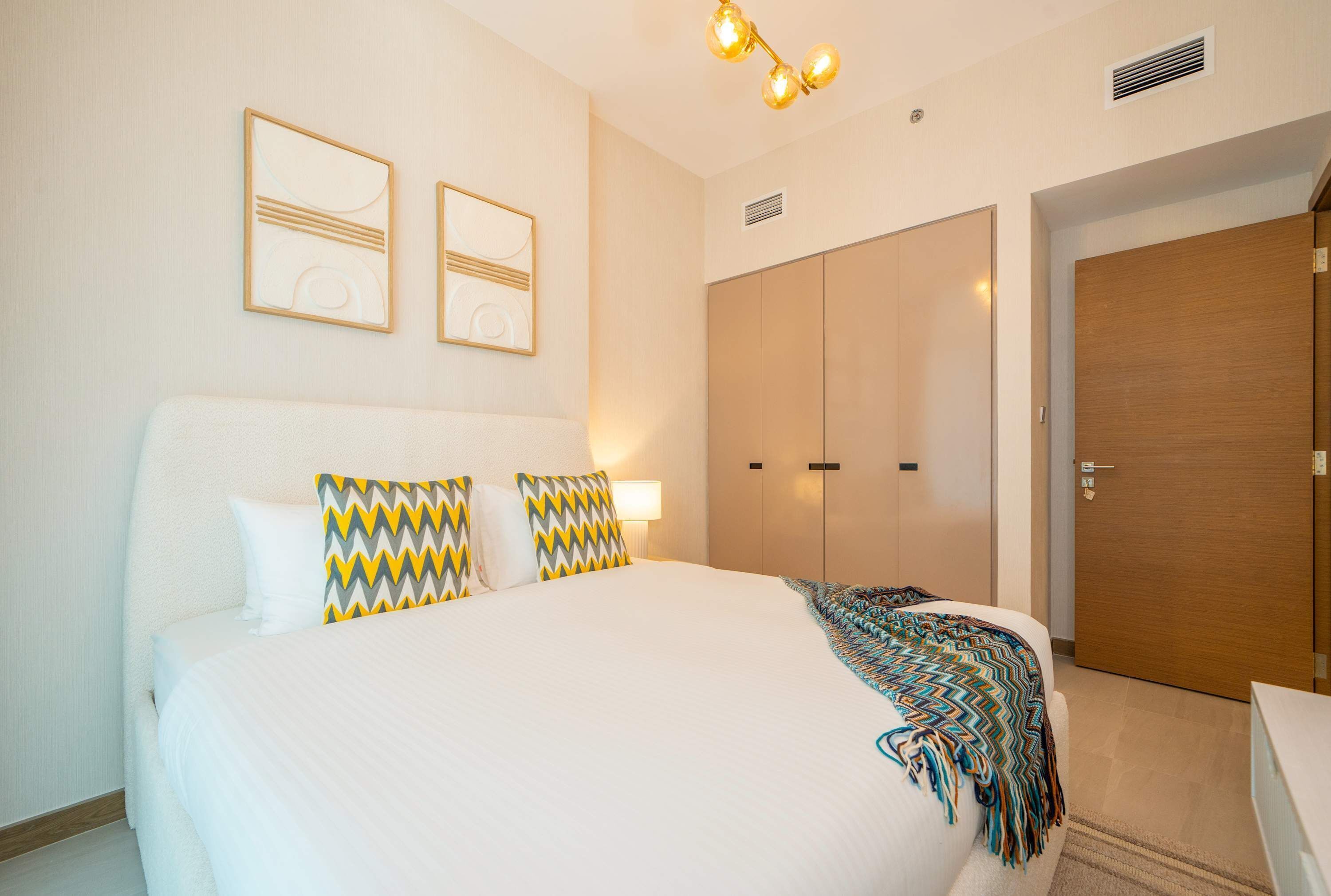 A hotel room with a large bed, a wardrobe, and two wall-mounted artworks.