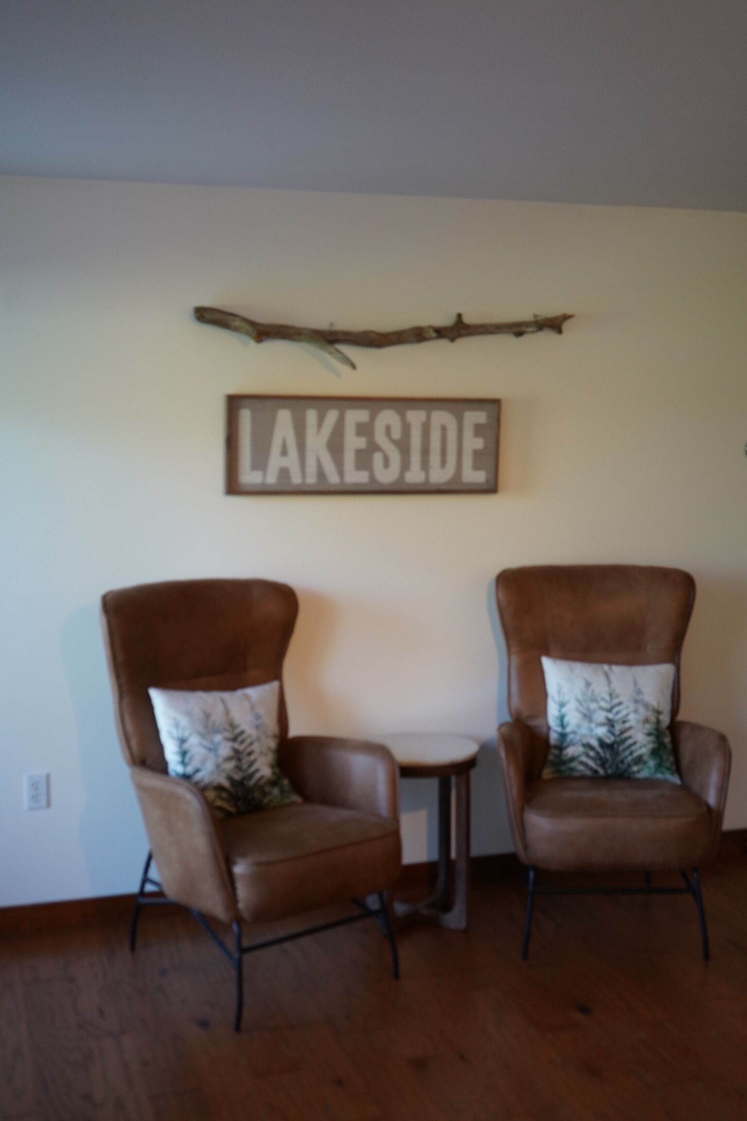 Two brown leather armchairs with matching pillows, a small wooden table, and a 'LAKESIDF' sign on the wall.