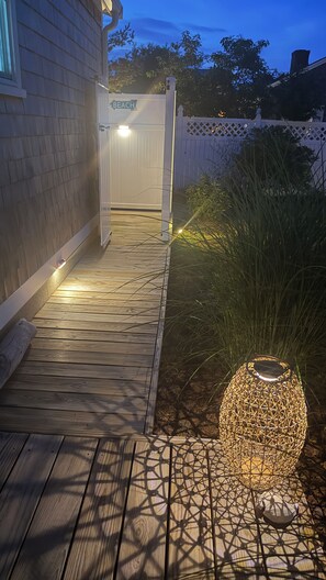 Una terraza de madera con un sendero que lleva a una reja blanca con la inscripción 'BEACH'.