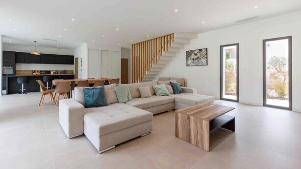 Un salon moderne avec un grand canapé d’angle, une table basse en bois et un escalier menant à un niveau supérieur.