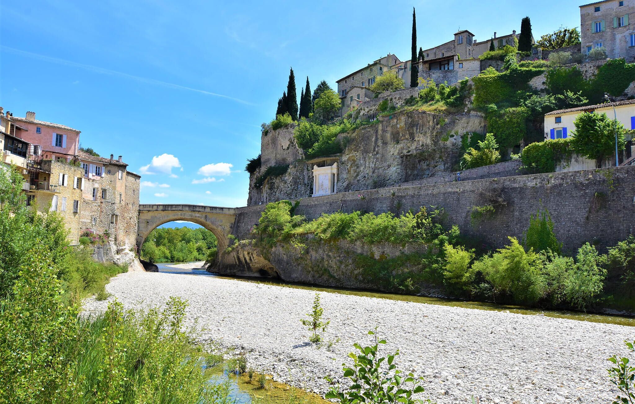 A stone bridge over a river, surrounded by buildings and greenery.