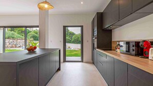 Une cuisine moderne avec des meubles de couleur sombre, un plan de travail en bois et une vue sur un jardin, visible à travers une porte vitrée.