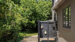 A wooden deck leading to a black metal outdoor toilet with two hanging planters. - Lovely home in Tranekær with WiFi (Tranekær)