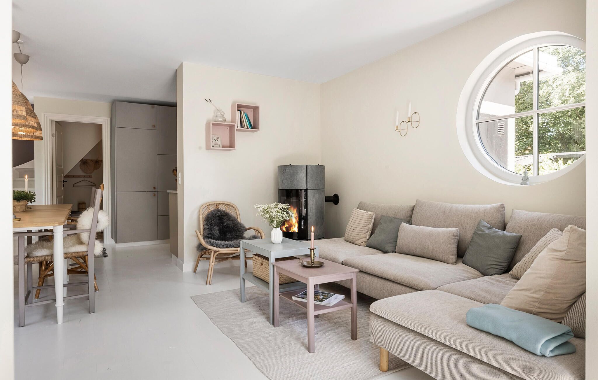 A cozy living room with a fireplace, a round window, and a dining area with a table and chairs.