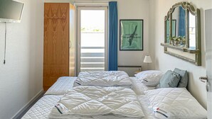 Et hotelværelse med seng, skab, et vindue med gardiner, et indrammet billede, et spejl og en lampe.