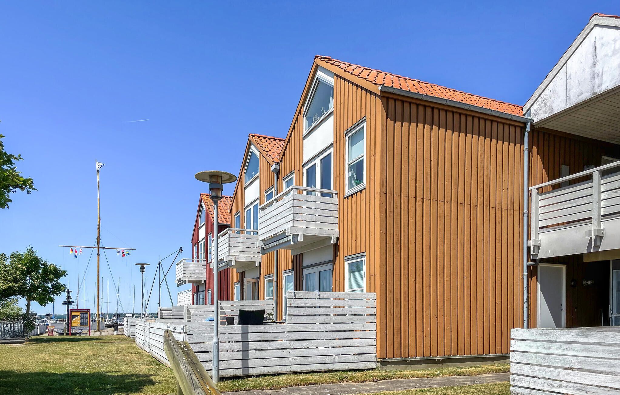 Een rij houten gebouwen met balkons, een heldere lucht en een jachthaven op de achtergrond.