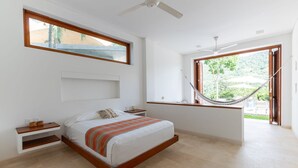 A modern bedroom with a large bed, a wooden nightstand, a small table, a hammock, and a large window with a view of greenery. - Yeguas U31 by Wynwood House (Anapoima)