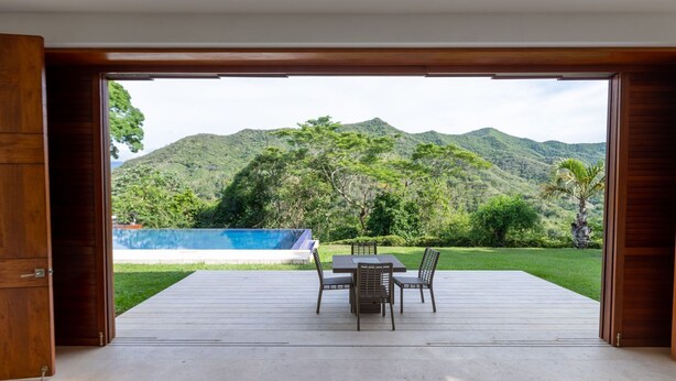 An open wooden door leading to a deck with a table and chairs, overlooking a pool and lush green hills. - Yeguas U31 by Wynwood House (Anapoima)