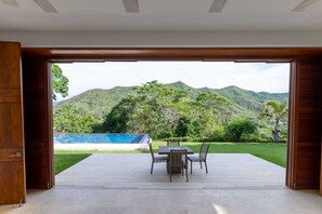 An open wooden door leading to a deck with a table and chairs, overlooking a pool and lush green hills. - Yeguas U31 by Wynwood House (Anapoima)