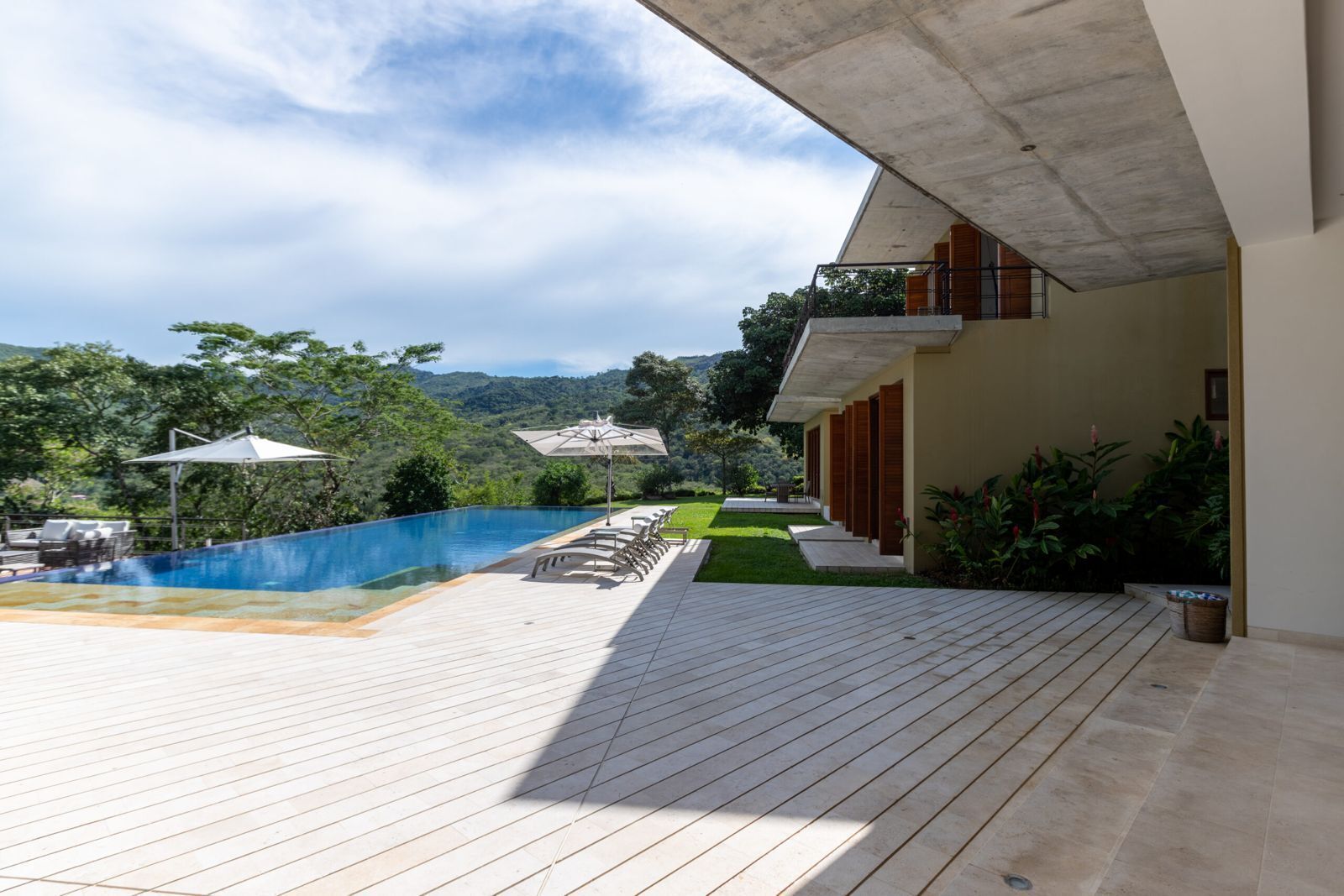 A modern outdoor pool area with a wooden deck, lounge chairs, and umbrellas.