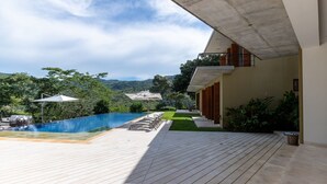 A modern outdoor pool area with a wooden deck, lounge chairs, and umbrellas. - Yeguas U31 by Wynwood House (Anapoima)