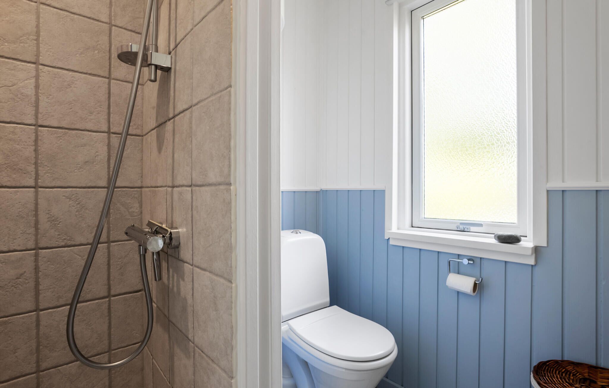 A bathroom with a shower, toilet, and a window.