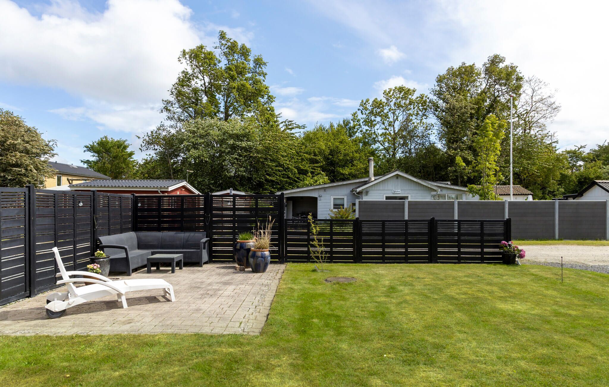 A backyard with a patio area, a fence, and a house in the background.