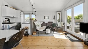 A modern kitchen with white cabinets, a dining area with a wooden table and chairs, and large windows offering a view of the outdoors. - 2 bedroom amazing home in Martofte (Martofte)