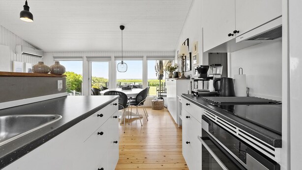 A modern kitchen with white cabinetry, a wooden floor, and a view to the outside. - 2 bedroom amazing home in Martofte (Martofte)