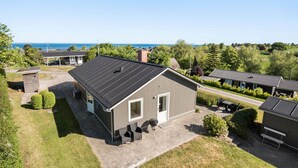 Ein zweistöckiges Gebäude mit flachem Dach, einer überdachten Terrasse mit Sitzgelegenheiten und Blick auf das Meer.