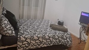 A bedroom with a bed, a small table, a chair, a TV, and a window with curtains. - Room for rent in a quiet house in the countryside (Bédarrides)