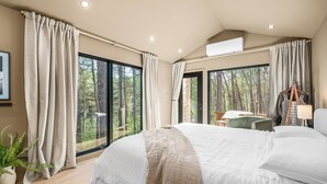 Un dormitorio con una cama grande, un escritorio y vistas a un bosque a través de amplios ventanales.