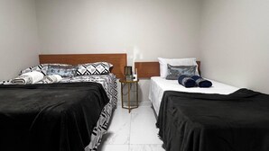 A bedroom with two beds, each with a black and white patterned bedspread, a wooden headboard, and a nightstand with a lamp between them.