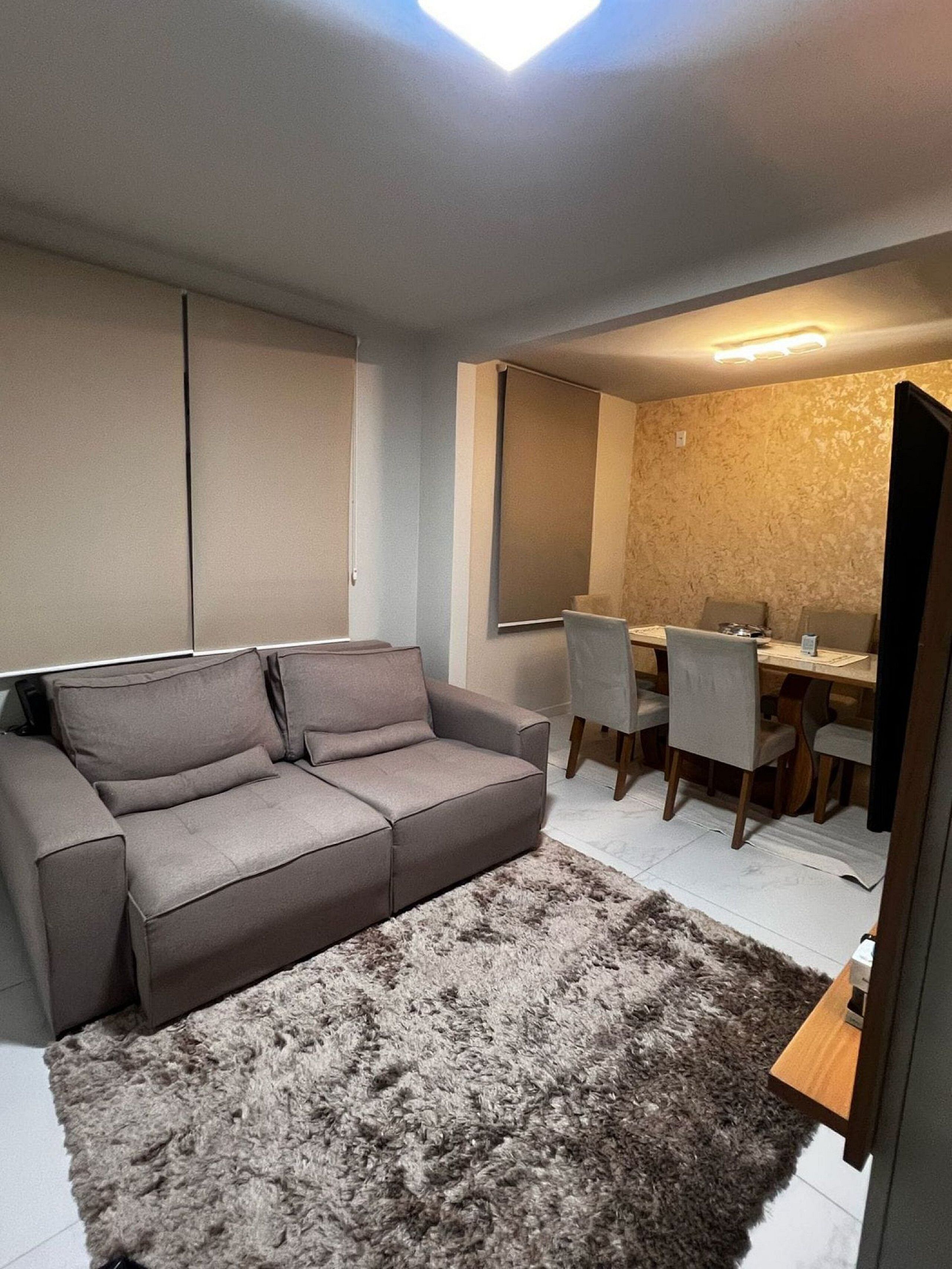 A modern living room with a grey sofa, a dining table with chairs, and a fluffy rug.