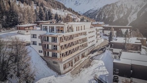Un hotel moderno con una estructura de varios pisos, situado en una zona montañosa nevada y con vistas a picos circundantes.