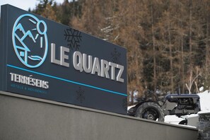 Un letrero para 'Le Quartz' con un logotipo que presenta una montaña y un sol estilizados, y el texto 'TERRÉSENS HOTELS & RESIDENCES'.