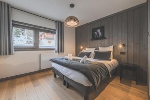 A bedroom with a large bed, a bedside table, a hanging light fixture, a window with curtains, and a framed picture on the wall. - Residence Terresens Le Quartz (Peisey-Nancroix)