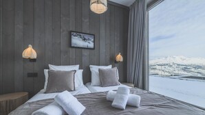 Un hotel moderno con una cama grande, dos lámparas fijadas a la pared, un cuadro enmarcado y vistas de montañas nevadas.