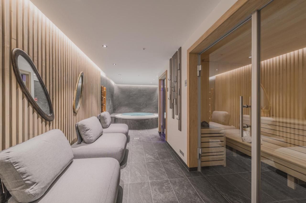 Un moderno espacio de spa con cabina de masajes, zona de relajación con bancos y una bañera de hidromasaje visible.