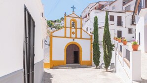 Une rue étroite bordée d’une petite église à la façade jaune et blanche, dotée d’une porte en bois et d’un clocher.