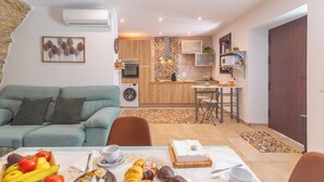 Una sala de estar con un sofá, una mesa de comedor con comida, una cocina con electrodomésticos y una puerta.