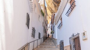 Una estrecha escalera de piedra que sube una colina empinada en una calle de paredes blancas, con barandales de metal y ventanas con rejas.