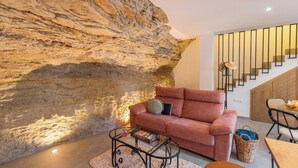 A modern living room with a stone wall, a pink sofa, a glass coffee table, and a staircase with wooden steps.