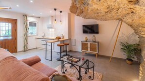 A modern living room with a sofa, a coffee table, a kitchen area with a dining table, and a TV mounted on the wall.
