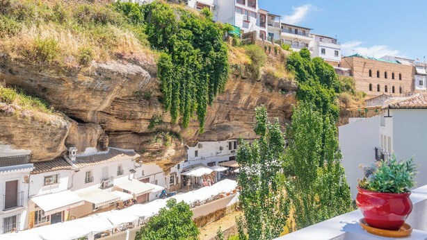 A coastal town with buildings on a cliff, a rocky landscape, and a potted plant on a balcony. - Bajo la Roca Setenil de las Bodegas by Ruralidays (Cádiz)