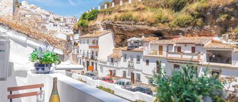 A balcony with a view of a coastal town, featuring white buildings, a cliff, and a potted plant.