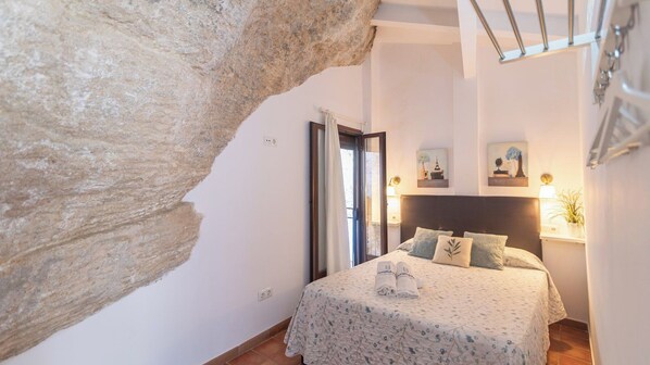 A bedroom with a bed, a headboard, a nightstand, a lamp, and a painting on the wall.