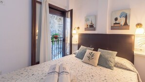 A hotel room with a bed, two bedside lamps, a nightstand, a window with curtains, and artwork on the walls. - Bajo la Roca Setenil de las Bodegas by Ruralidays (Cádiz)