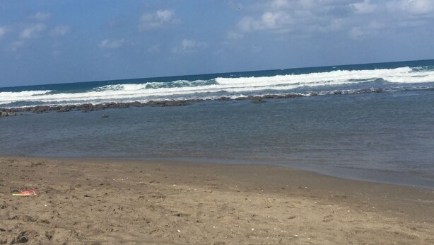 Ein Strand mit Wellen, blauem Himmel und felsiger Küste.