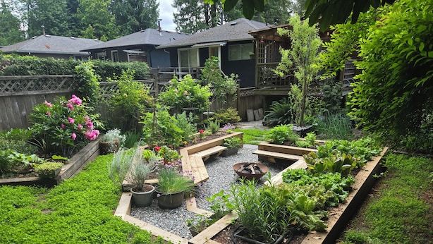 A garden with raised beds, a fire pit, and a wooden deck.