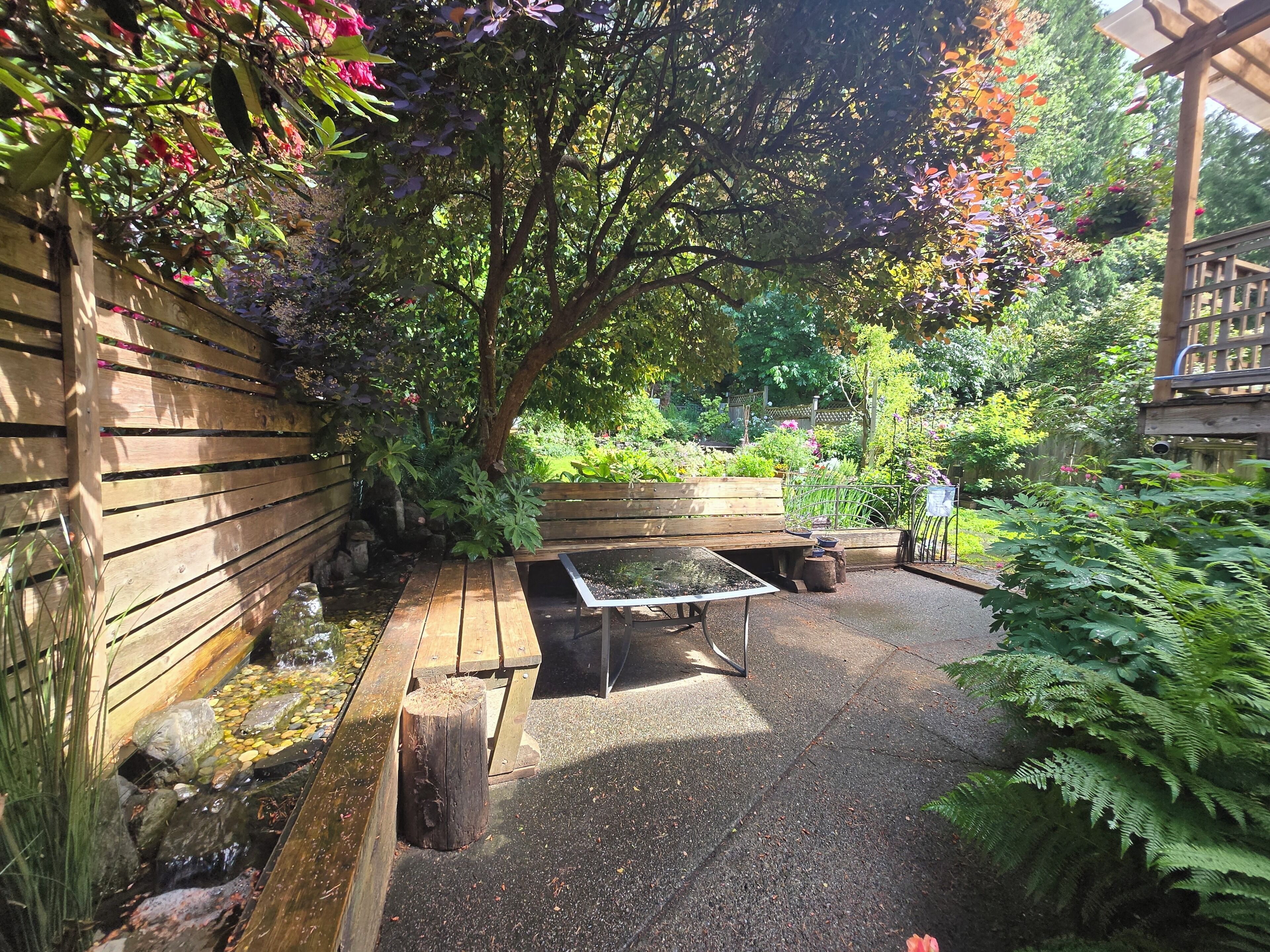 A wooden bench, a small table, and a garden area with various plants and a wooden fence.