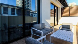 Uma área de estar ao ar livre com mobiliário moderno, uma parede de vidro e vista para a paisagem urbana.