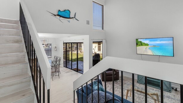 A spacious interior with a staircase, a dining area, and a TV displaying a beach scene.